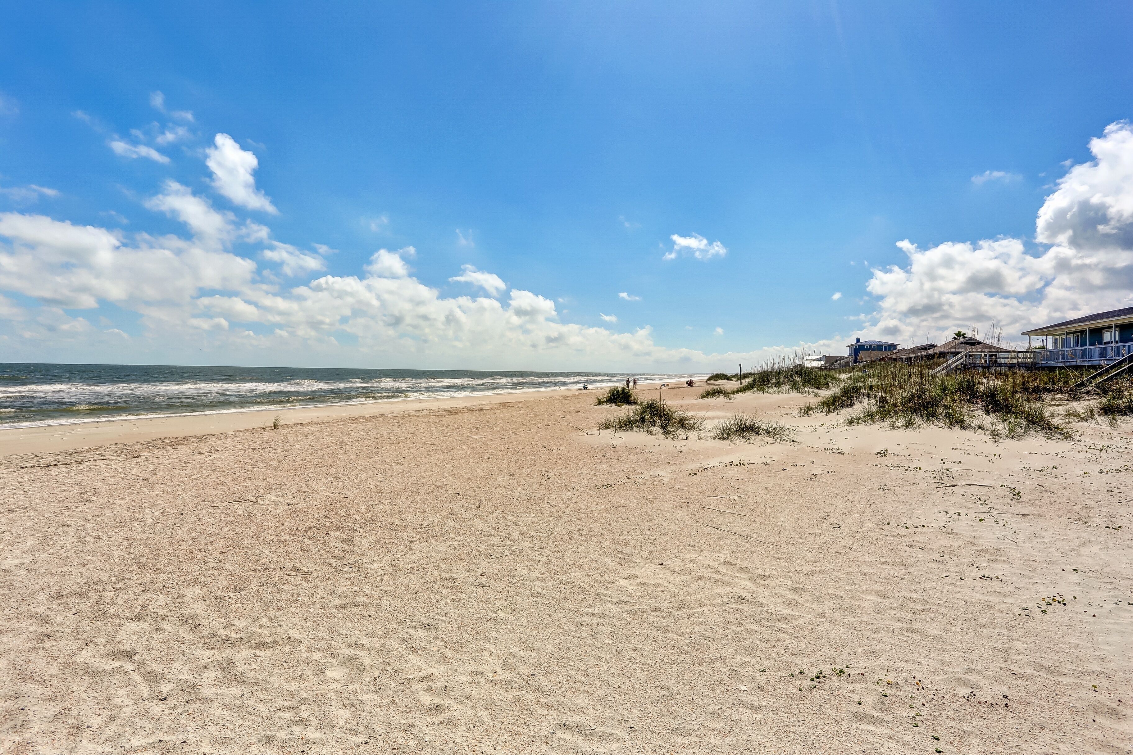 A beach with a clear sky, a sandy shore, and a building with a balcony.