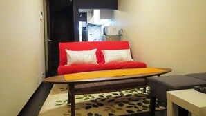 Une petite pièce agréable, dotée d’un canapé rouge, d’une table basse en bois et d’une petite table blanche.