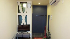 Une pièce décorée d’un grand motif en forme de « X » sur un mur, dotée d’un téléviseur à écran plat, d’un petit coin salon et d’une table avec un set de table jaune.