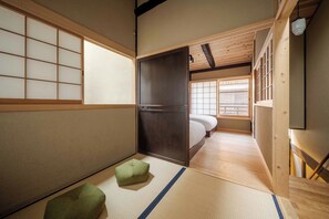 Een traditionele Japanse kamer met tatami vloeren, een futon bed, glijdende deuren en een klein groen kussen.