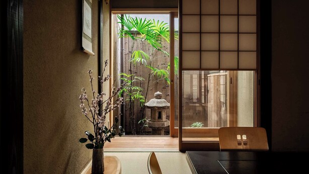 Una habitación japonesa tradicional con suelo de tatami, un divisor shoji y vistas a un jardín de bambú por una puerta corredera.