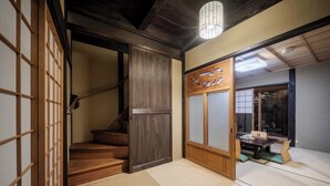 Un interior japonés tradicional con suelo de tatami, una escalera de madera, puertas correderas y un comedor con mesa y sillas.
