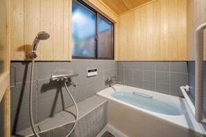 Een badkamer met een badkuip, douche en houten wanden.