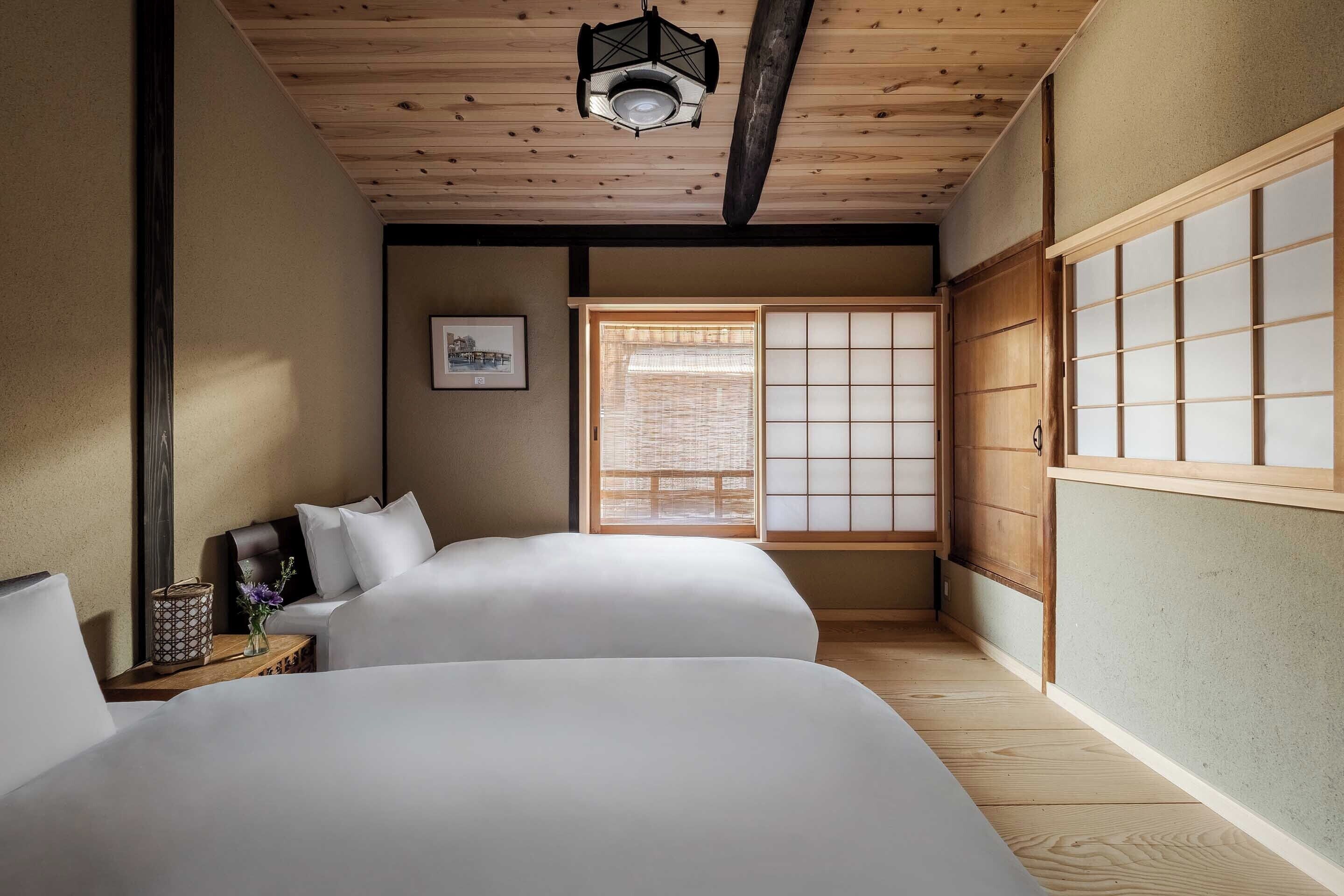 A traditional Japanese-style room with two beds, a wooden ceiling, a shoji screen, and a hanging lantern.