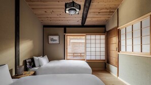 Una habitación tradicional japonesa con dos camas, techo de madera, un shoji y un farol colgante.