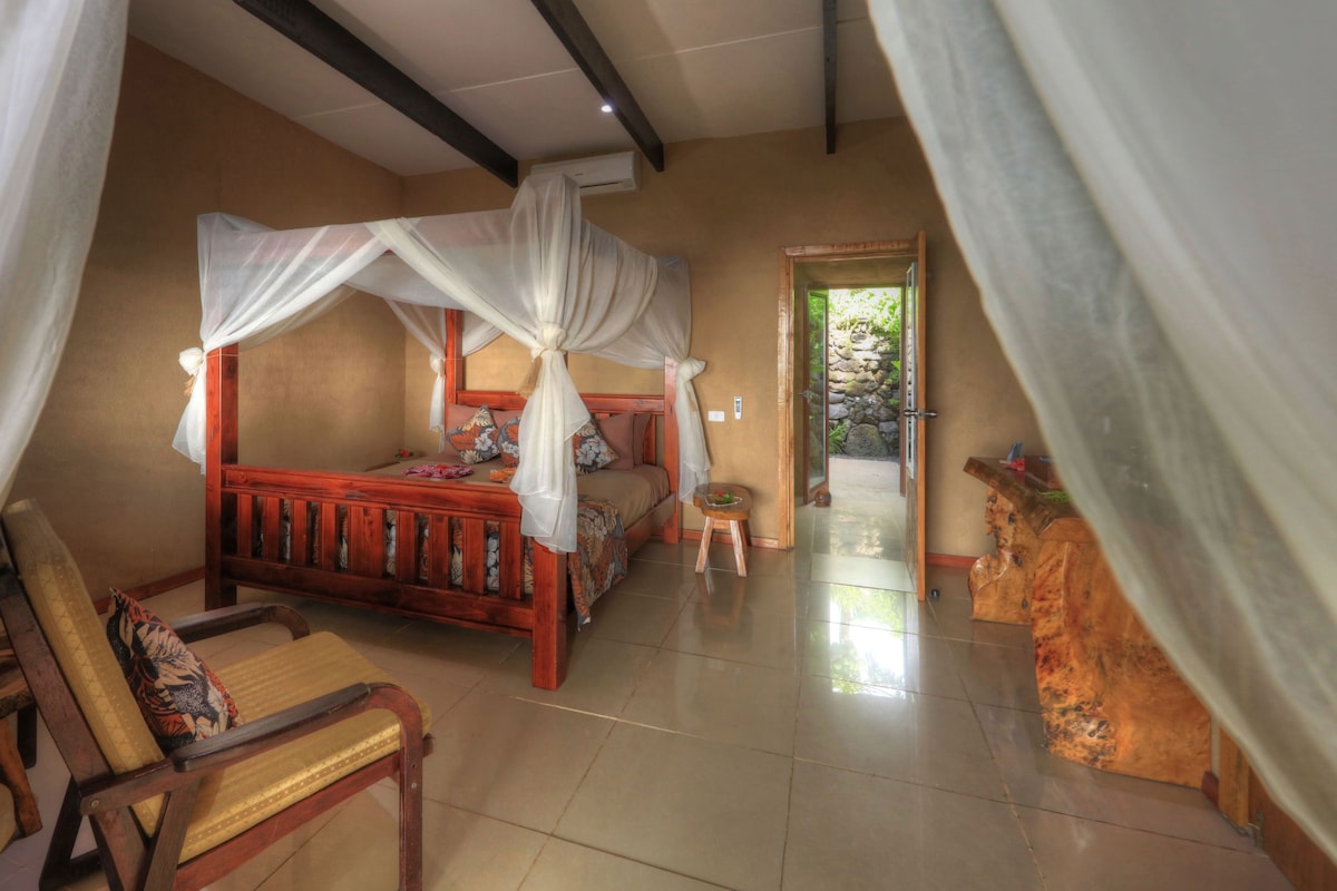 A bedroom with a four-poster bed, a wooden chair, and a small table.