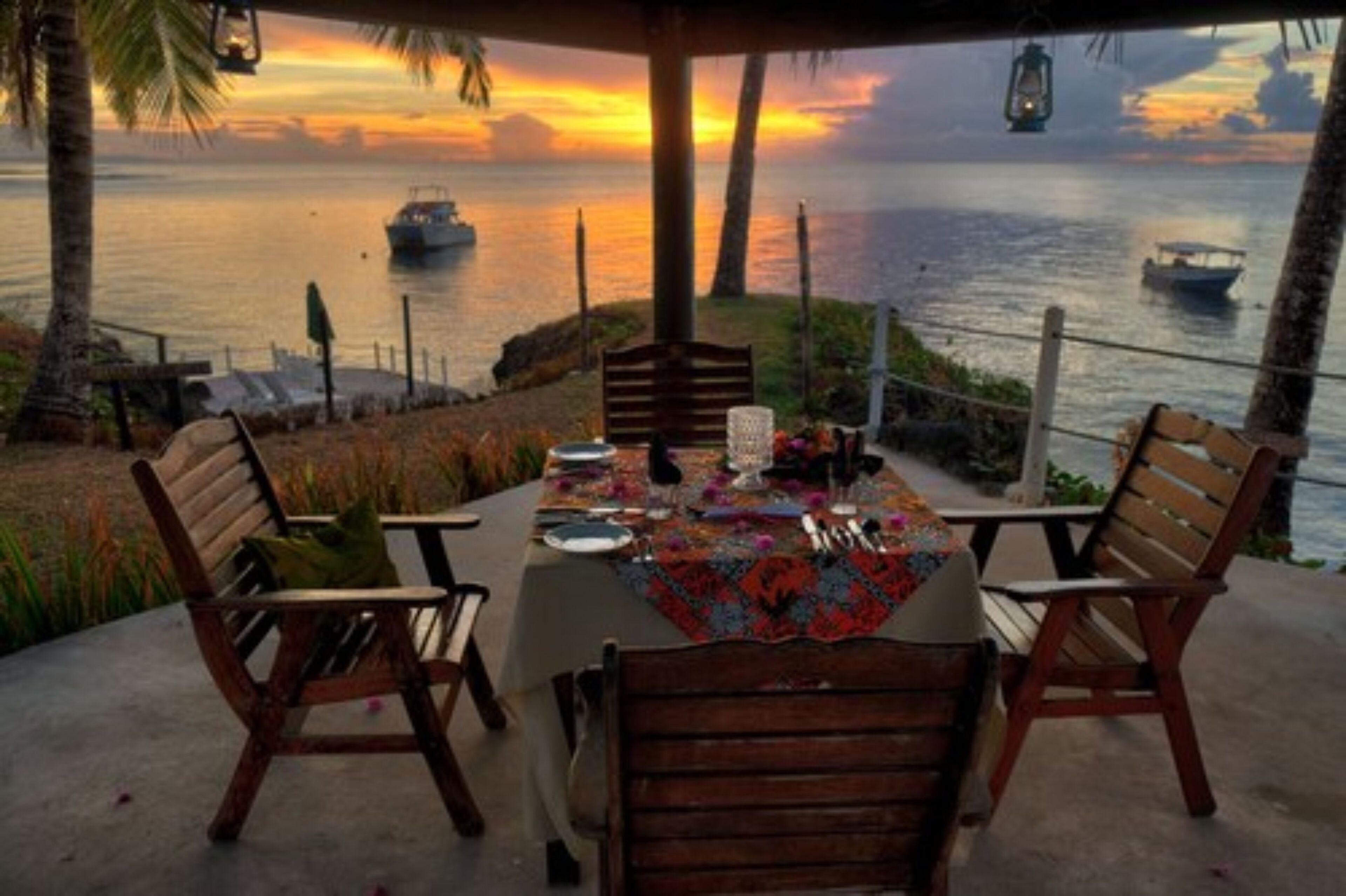 Un área de comedor al aire libre con una mesa preparada para dos, con vista a un cuerpo de agua y barcos.