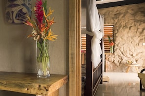 A room with a wooden bench, a vase with flowers, a bed with white curtains, and a stone wall. - Paradise Taveuni (Taveuni Island West)
