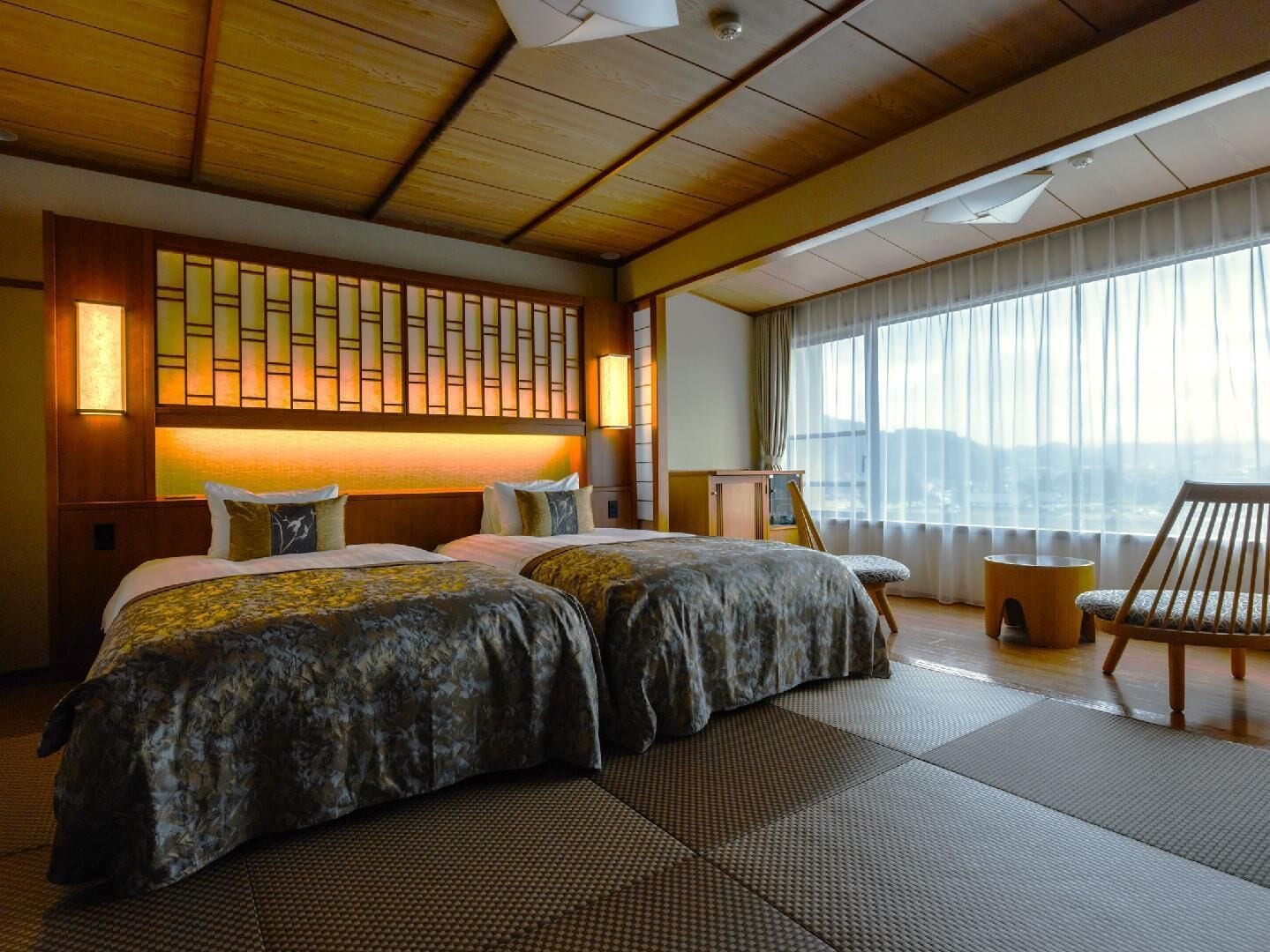 A hotel room with a large bed, a wooden ceiling, a view of the city, and a traditional Japanese-style wall.