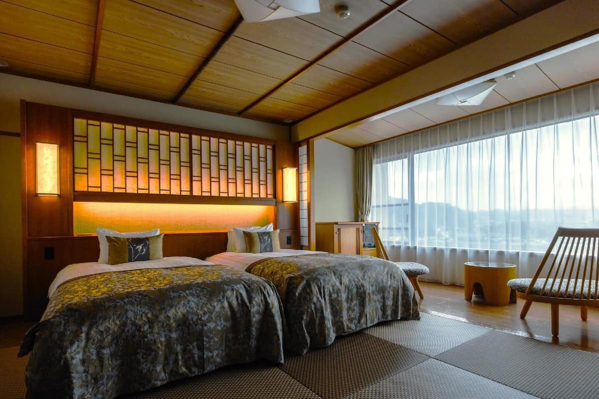 Een hotelkamer met een groot bed, een houten plafond, uitzicht op de stad en een traditionele Japanse wand.