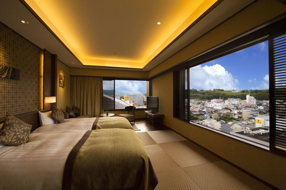 Een hotelkamer met twee bedden, een televisie, een tafeltje en uitzicht op een stadsbeeld.