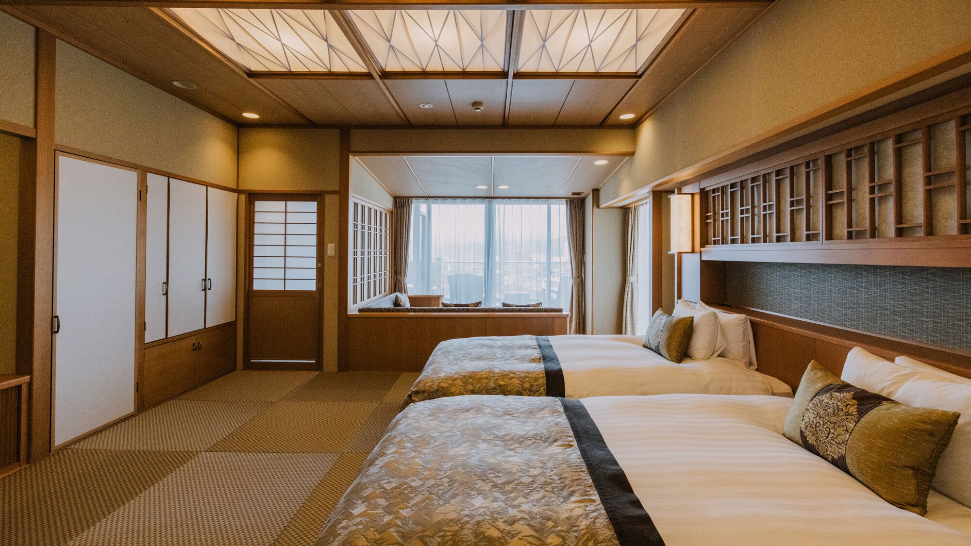 A hotel room with two beds, a view of the city, and traditional Japanese decor.