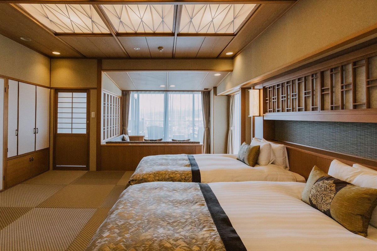 Een hotelkamer met twee bedden, uitzicht op de stad en traditionele Japanse decoratie.