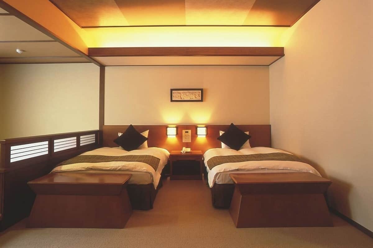 Een hotelkamer met twee eenpersoonsbedden, een klein tafeltje en een wandlamp.