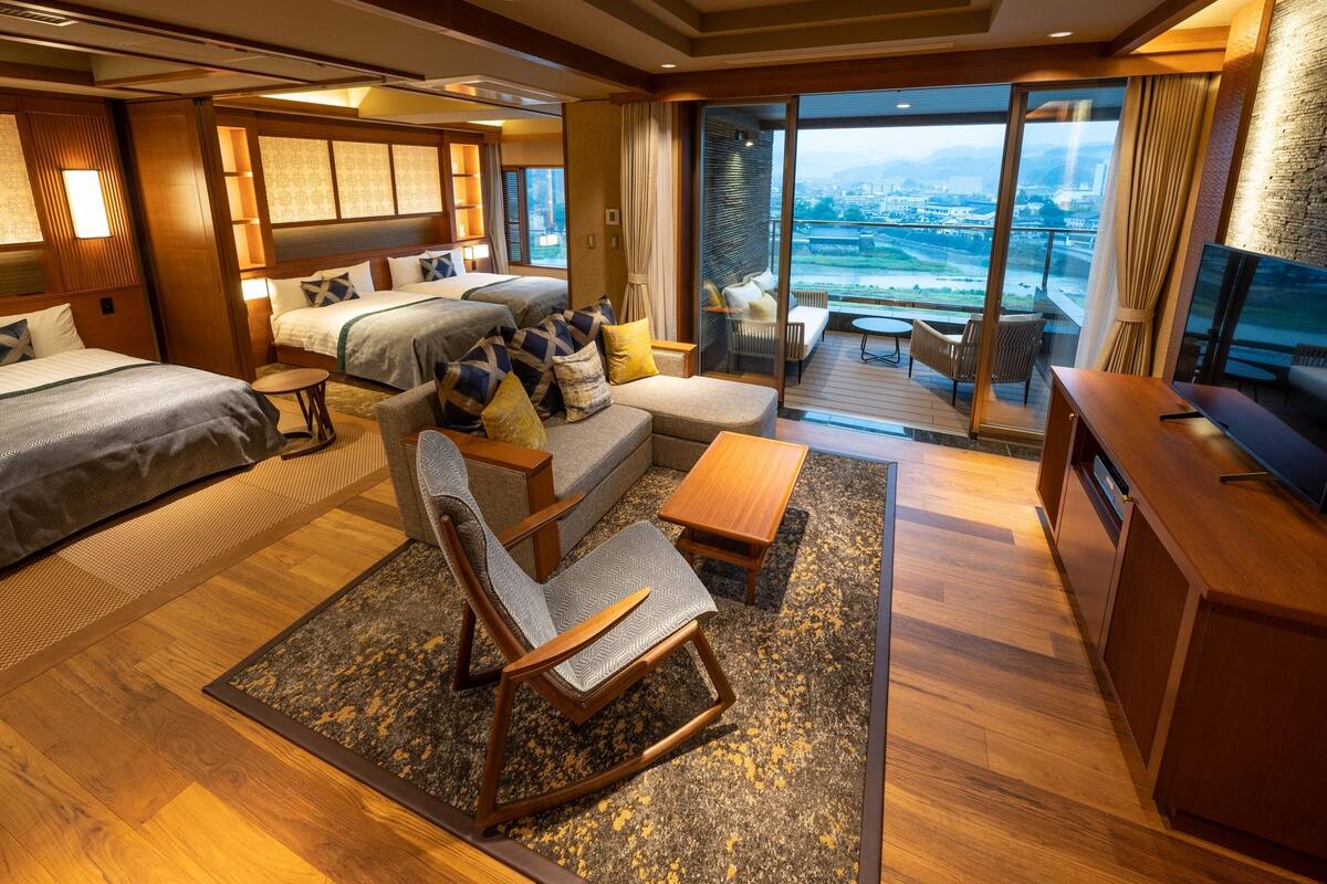 Een moderne hotelkamer met twee bedden, een bank, een televisie en een balkon met uitzicht op de stad.