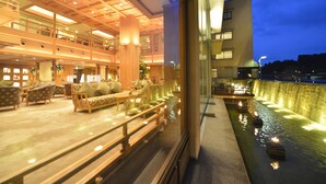 Eine Hotellobby mit Sitzbereichen, einer Wasserspiels und Blick auf das äußere Gebäude.