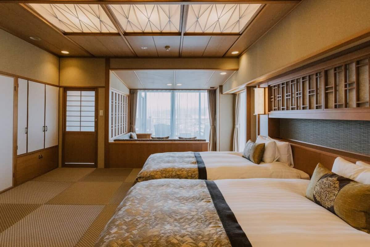 Een hotelkamer met twee bedden, een groot raam en traditionele Japanse schuifdeuren.