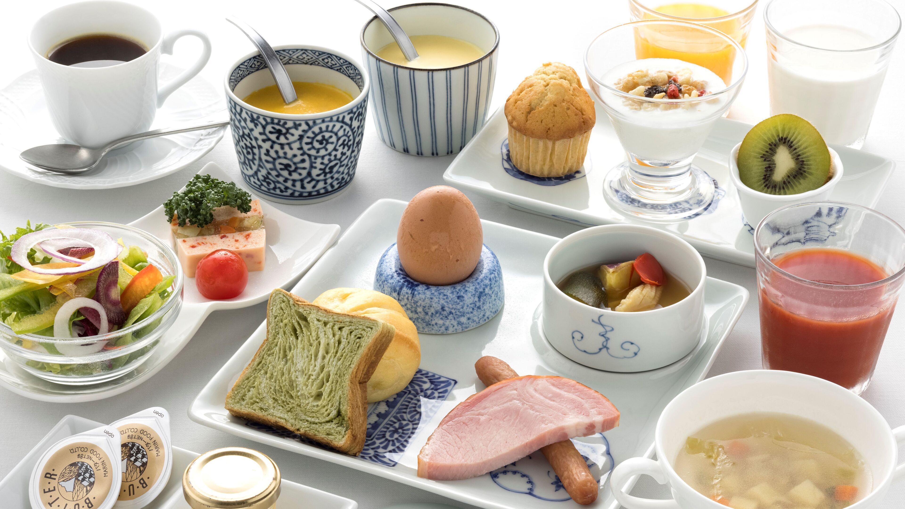 A breakfast table with various food items including toast, ham, soup, and a muffin.