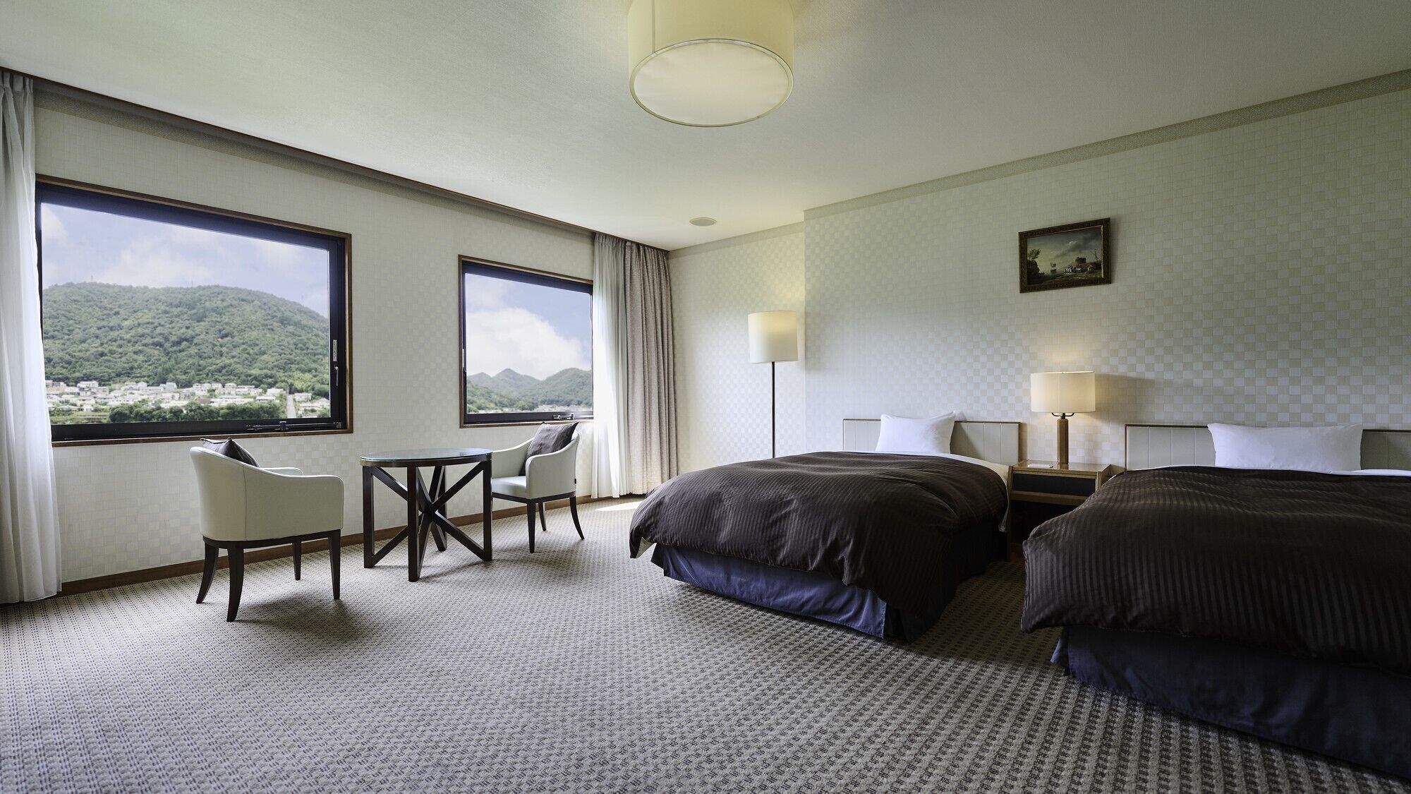 A hotel room with a bed, a desk, a chair, and a view of a mountainous landscape.