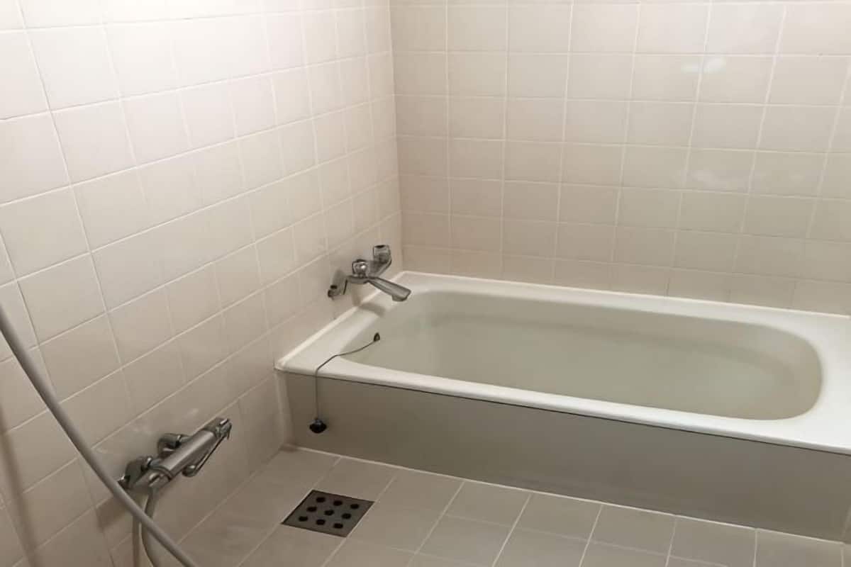 A bathroom with a bathtub, white tiled walls, and a shower area.
