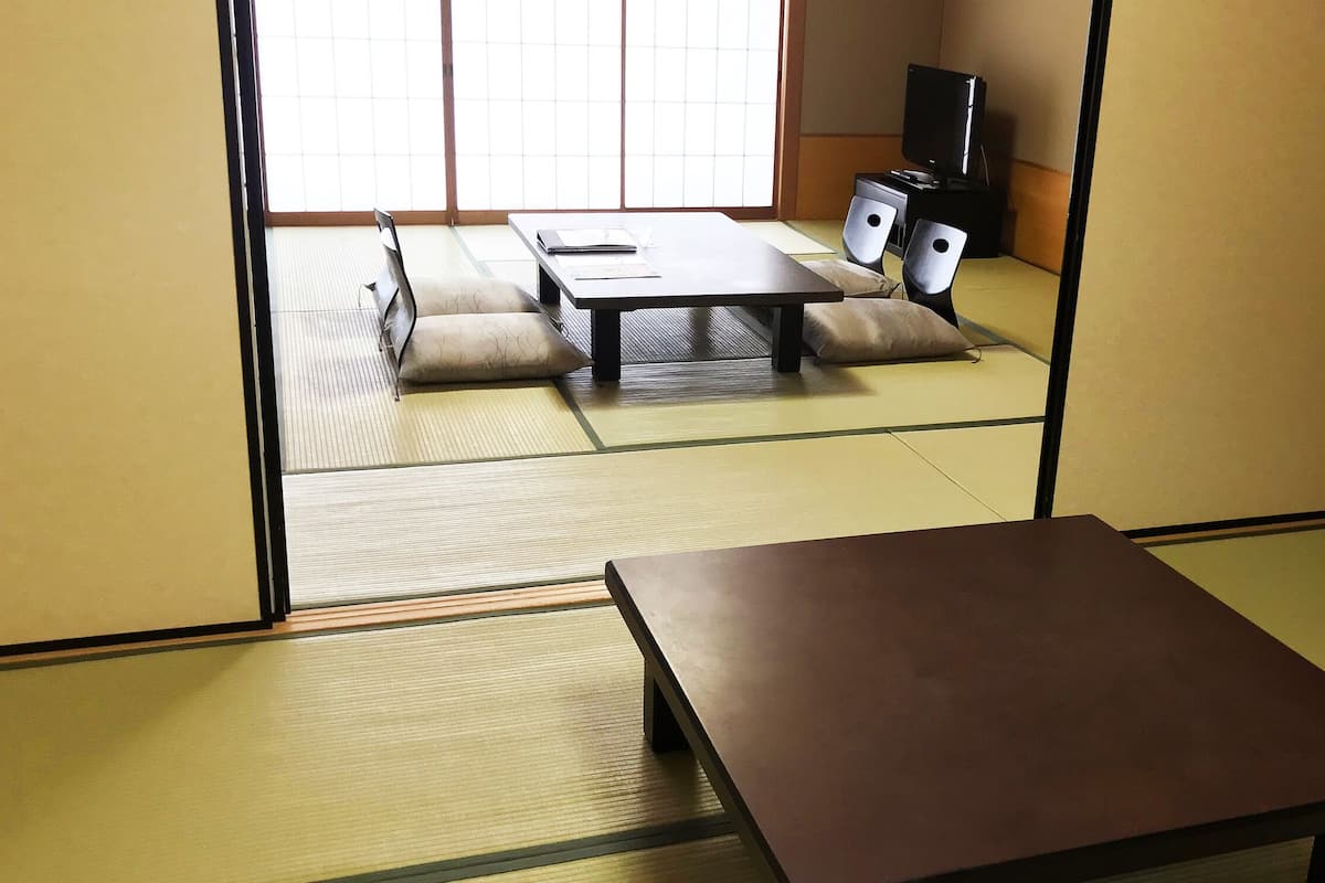 Una habitación con tatami, una mesa baja, cojines y un televisor sobre un soporte.