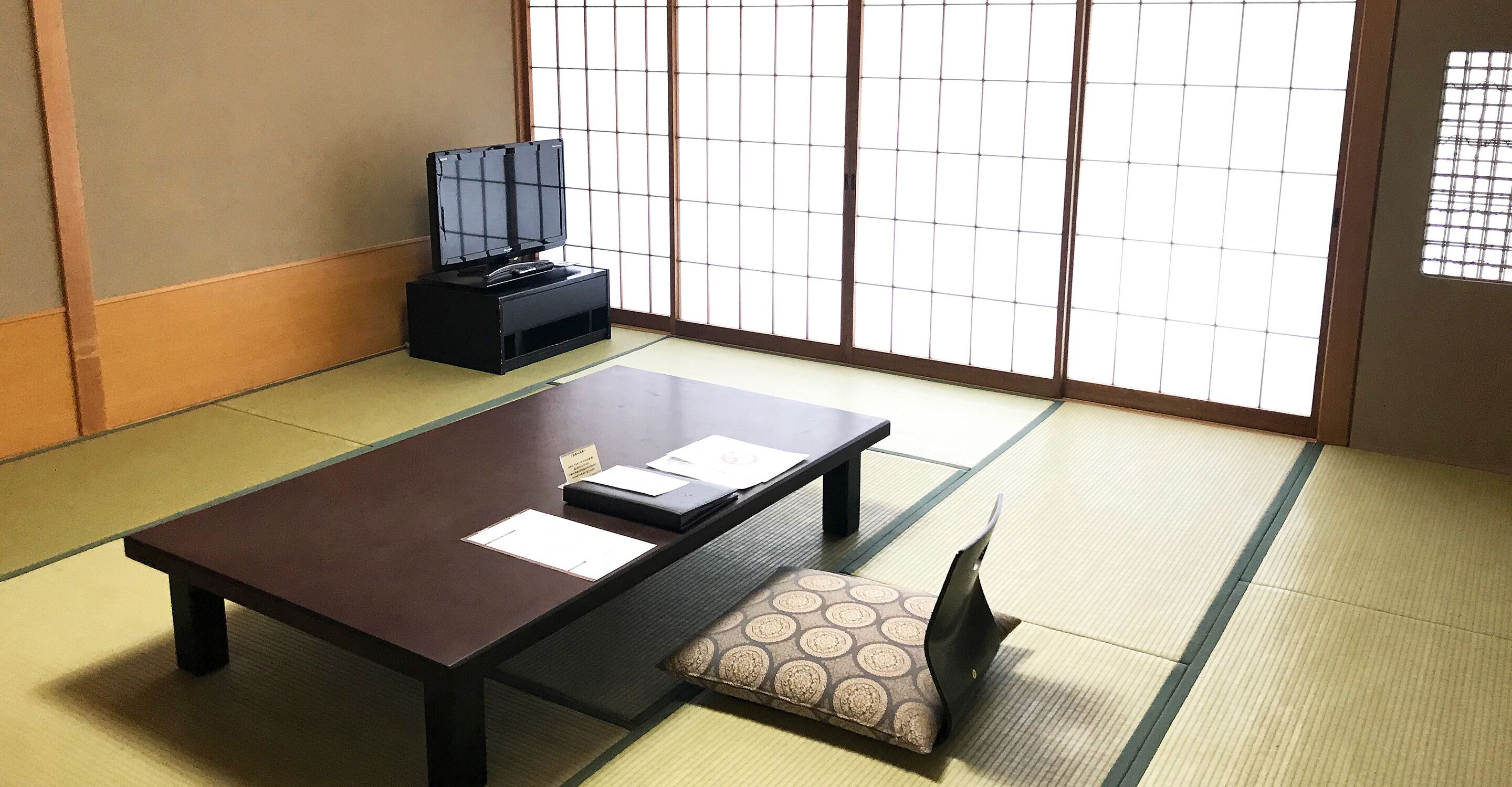 A traditional tatami room with a low table, a cushion, and a television on a stand.