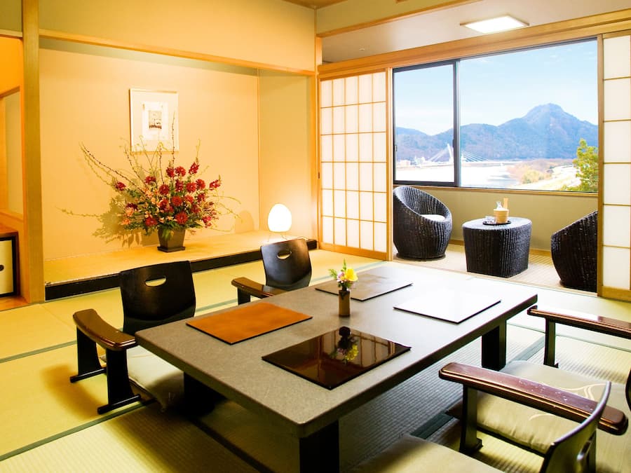 A traditional Japanese room with tatami flooring, a low table with cushions, and a view of mountains through a shoji screen.