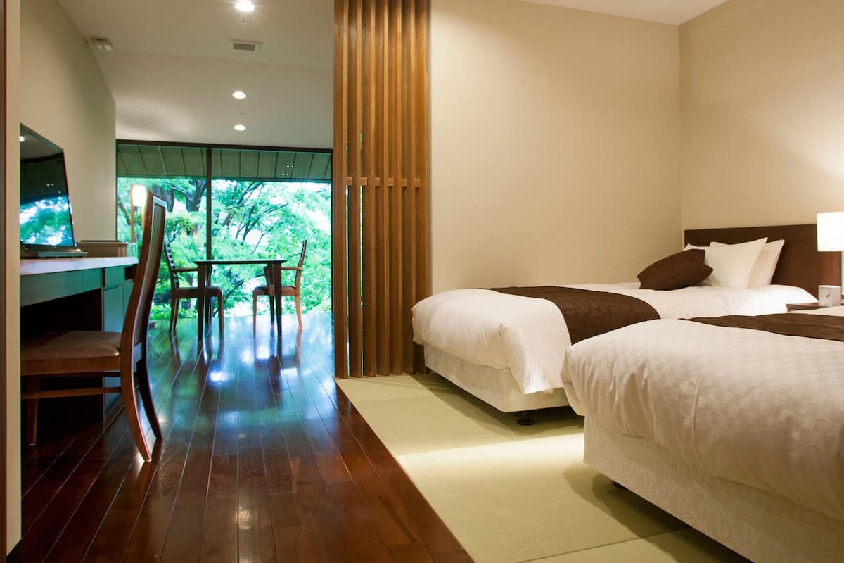 Habitación de hotel con dos camas, un escritorio con silla y vistas a zonas verdes.