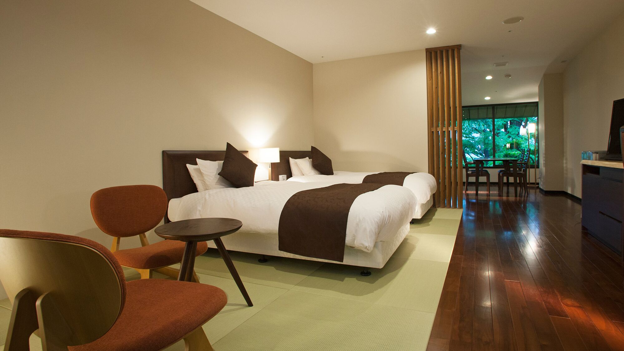 A modern hotel room with a large bed, a desk, and a view of greenery.