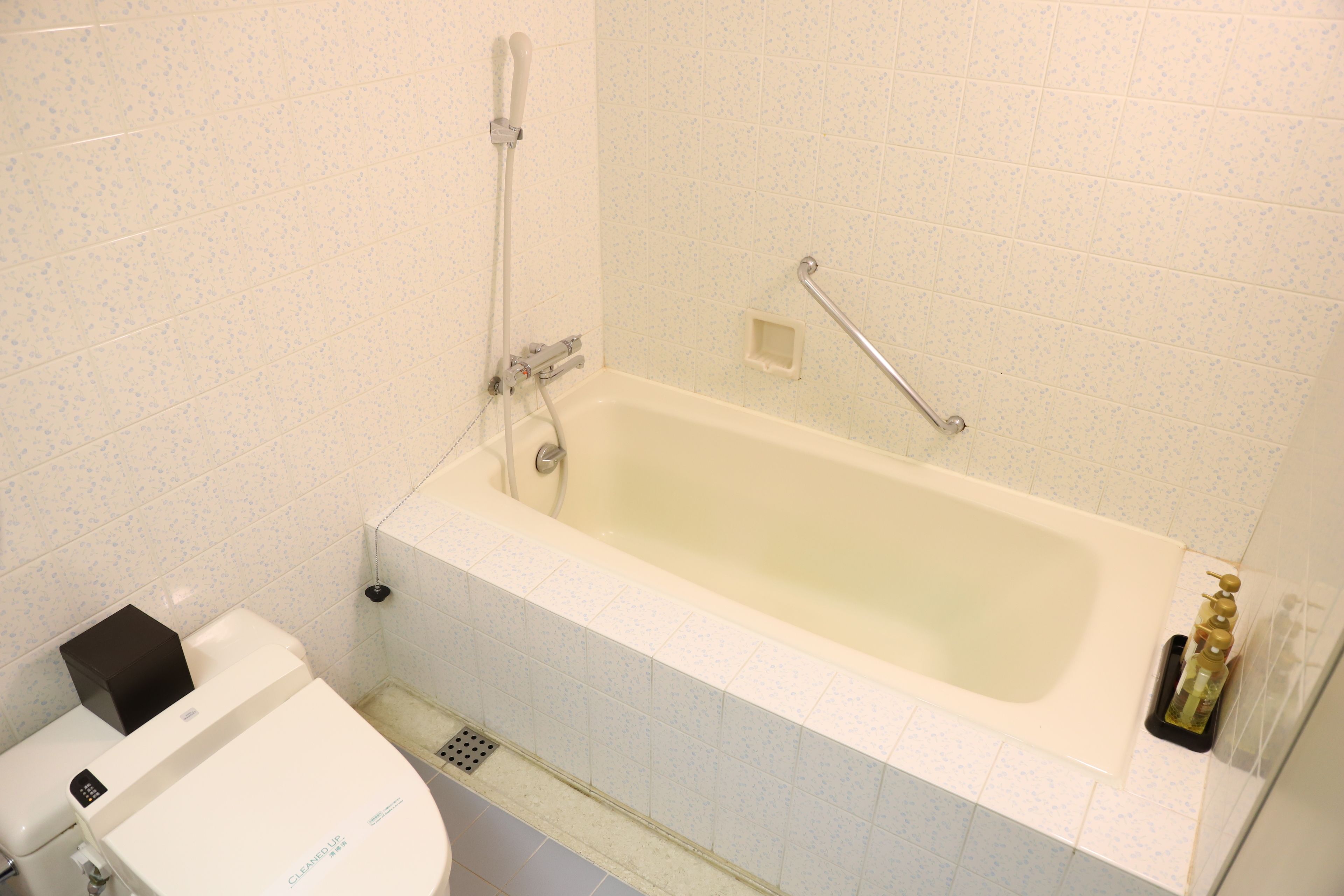 A bathroom with a bathtub, toilet, and a handrail.
