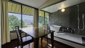 A modern bathroom with a bathtub, shower, and large windows offering a view of greenery and mountains.