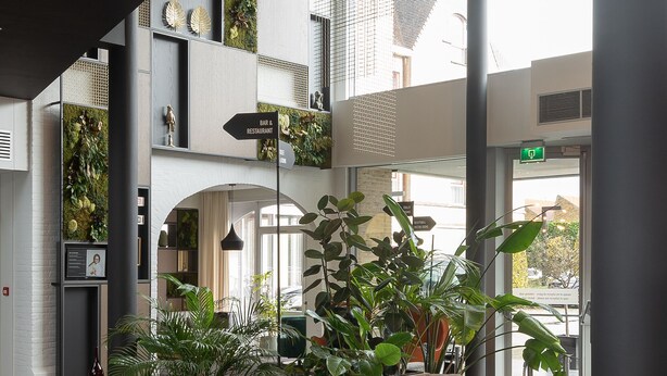 Un vestíbulo moderno con un sofá seccional gris, plantas de interior y un cartel que indica un bar y restaurante.