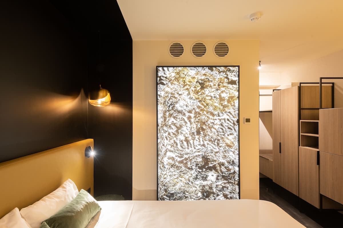 A modern bedroom with a bed, a wall-mounted light, a frosted glass door, and built-in wooden cabinets.