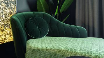 A modern living room with a green sofa, a patterned ottoman, and a large plant.