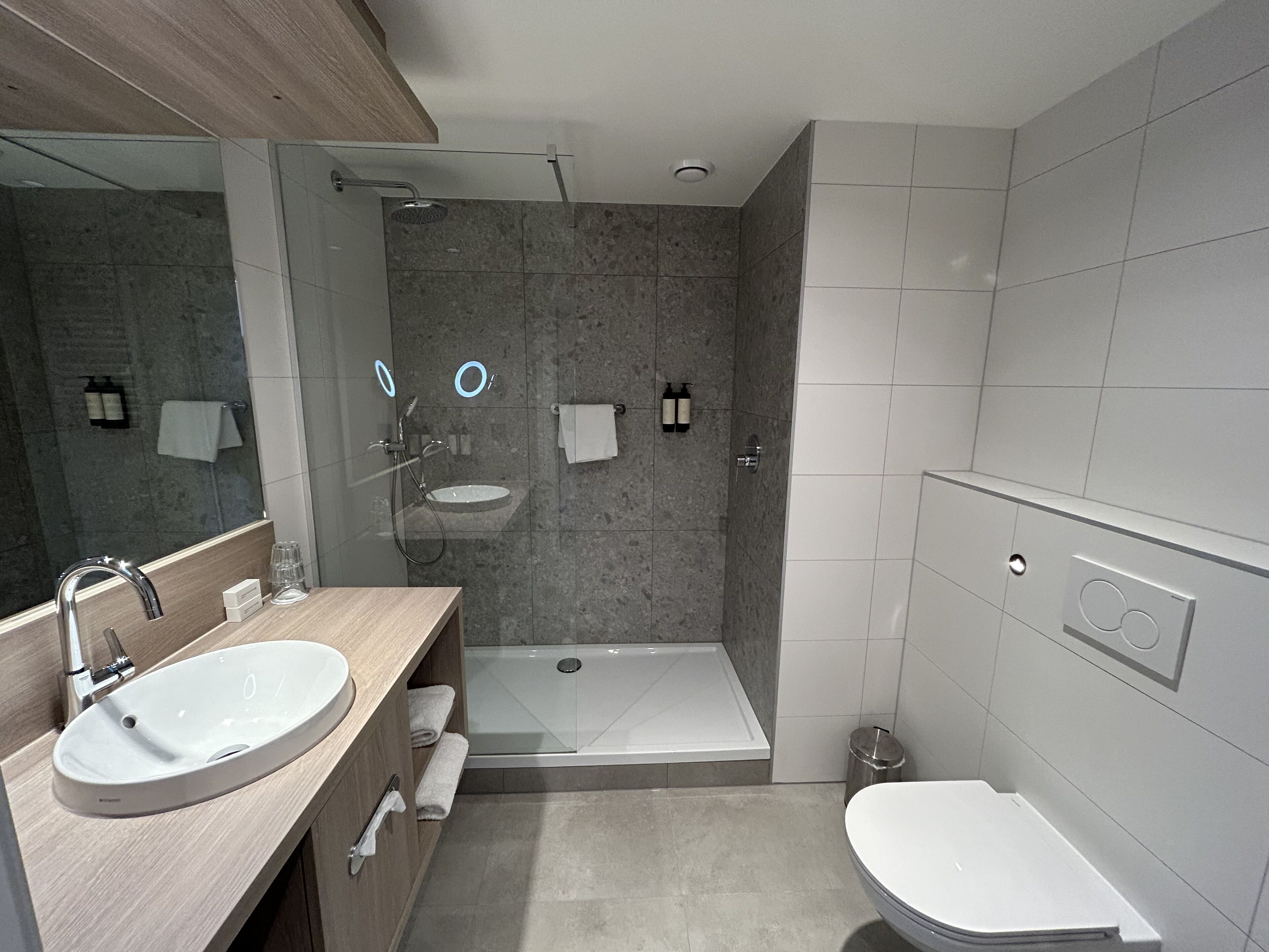Un baño moderno con lavamanos doble, un espejo grande, ducha e inodoro.