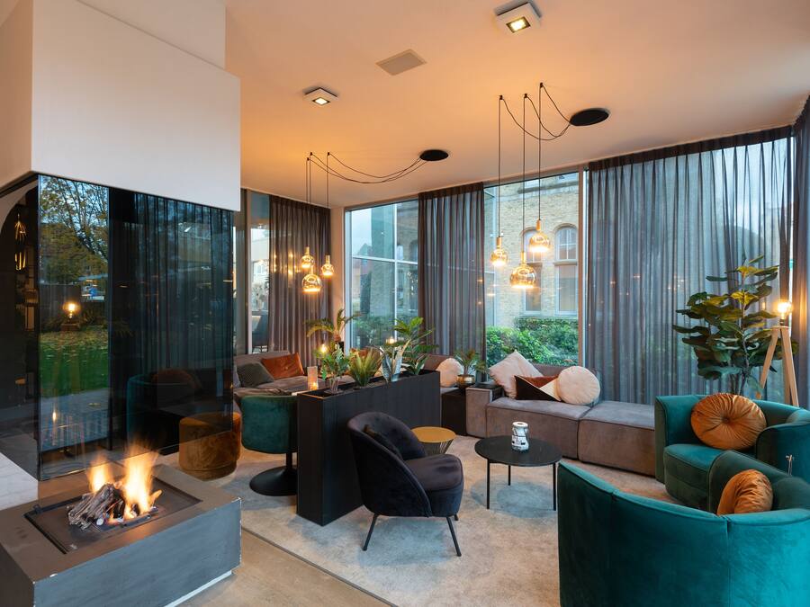 A modern living room with a fireplace, comfortable seating, and large windows offering a view of the outdoors.