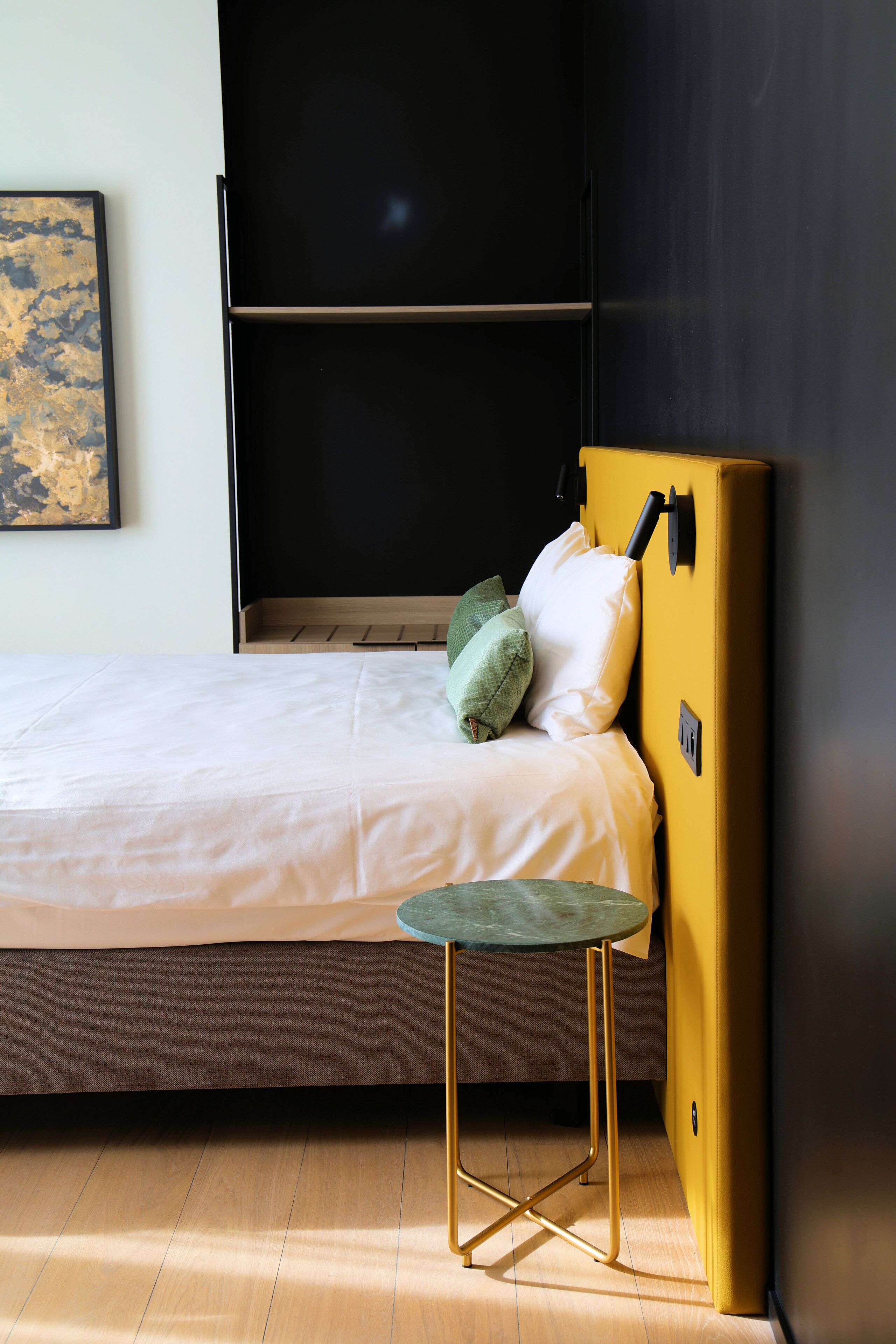 Une pièce avec un lit, une armoire jaune, une petite table et un tableau accroché au mur.