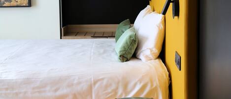 Una habitación con una cama, un armario amarillo, una mesita y un cuadro en la pared.