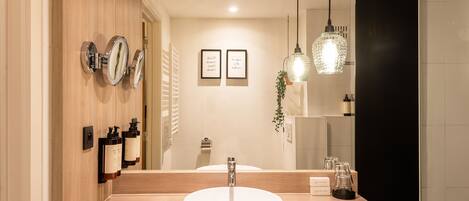 Un baño moderno con tocador de madera, un lavabo redondo y dos repisas para toallas.