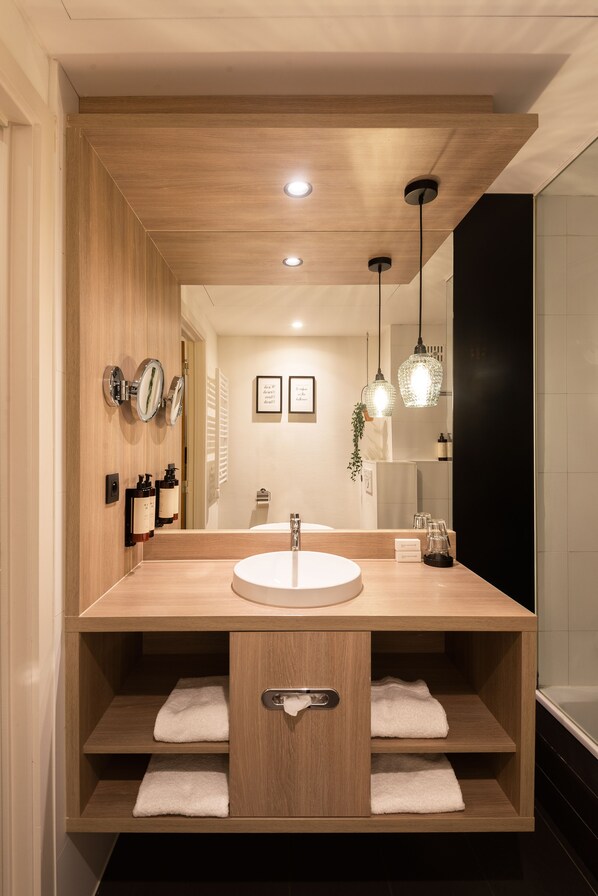 A modern bathroom with a wooden vanity, a round sink, and two towel shelves.