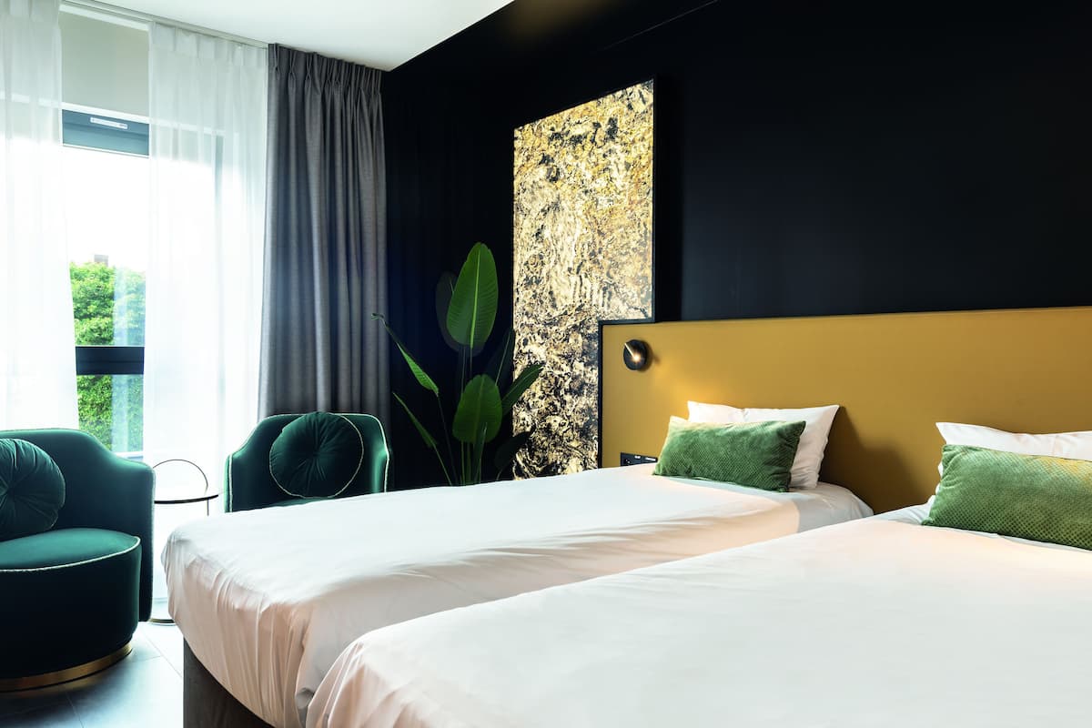 A hotel room with two beds, a large abstract painting on the wall, a green plant, and a view of greenery outside.