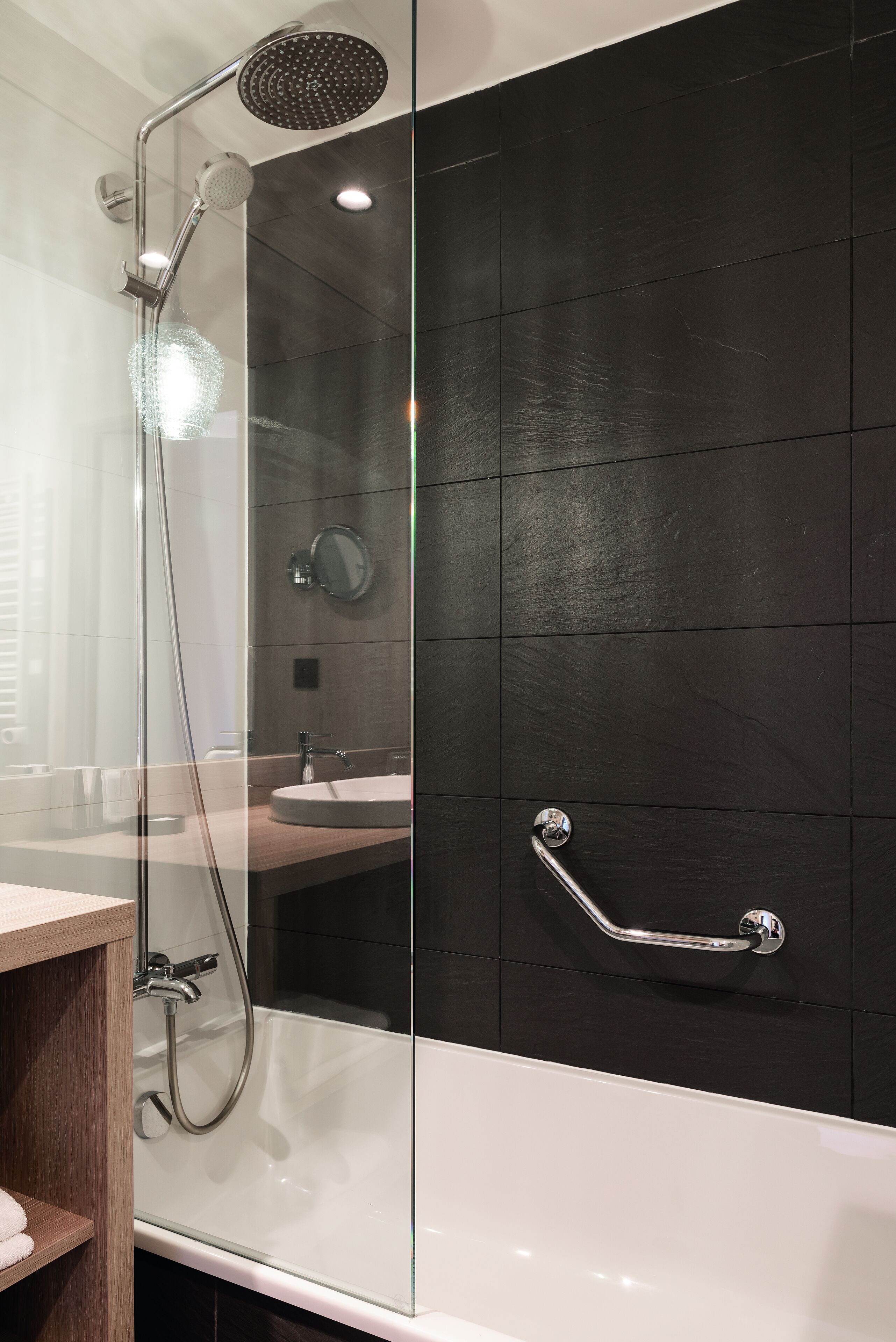 A modern bathroom with a glass-enclosed shower, a white bathtub, and a wooden vanity.