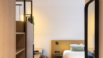 Una habitación de hotel moderna con cama, escritorio, silla, mesita de noche y espejo.