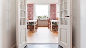 A spacious room with a large window, a dining area with a table and chairs, and a patterned wall. - Bläsinge Gård Kullabygden - Hostel (Jonstorp)