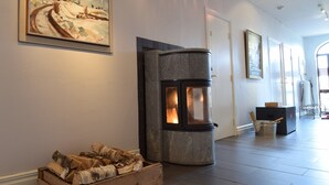 A room with a fireplace, a painting on the wall, and a wooden box with logs. - Bläsinge Gård Kullabygden - Hostel (Jonstorp)