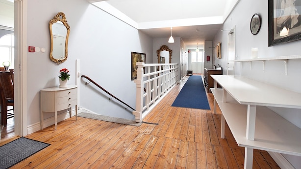 A hallway with wooden flooring, white walls, a white bench, and a staircase with a white railing. - Bläsinge Gård Kullabygden - Hostel (Jonstorp)