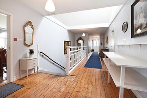 A hallway with wooden flooring, white walls, a white bench, and a staircase with a white railing. - Bläsinge Gård Kullabygden - Hostel (Jonstorp)
