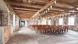 A spacious hall with wooden beams and stone walls, featuring a long table with chairs arranged for dining. - Bläsinge Gård Kullabygden - Hostel (Jonstorp)