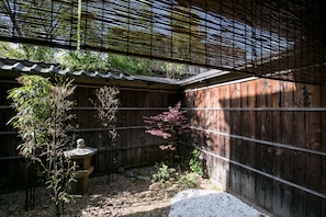 A traditional Japanese garden with a wooden fence, a stone lantern, and various plants.