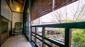 A room with a sliding door leading to a balcony, a chair, and a view of a garden and buildings outside. - KYOTO yadomachi Kamishichiken (Kyoto)